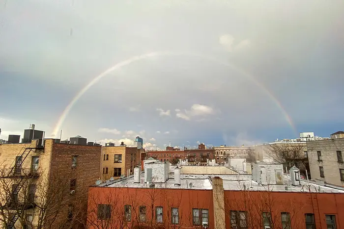 A complete shot of a rainbow over New York City buildings on a drizzly afternoon.